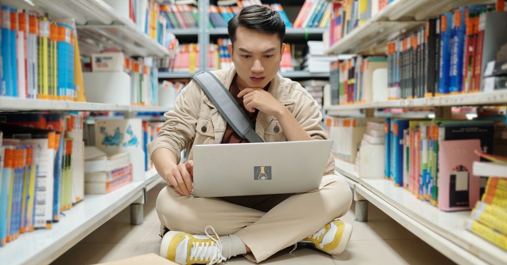Estudante de iniciação científica lendo artigos em inglês em um computador na biblioteca